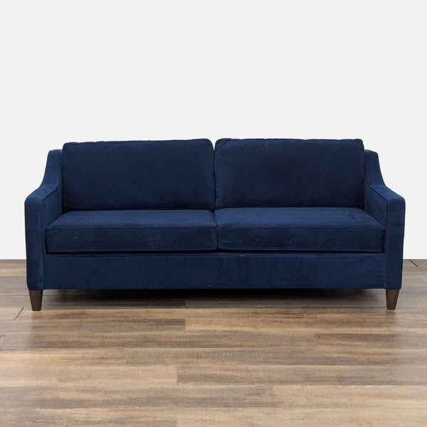 Dark blue velvet West Elm sleeper sofa with wood legs, viewed from the front, set on a wooden floor.