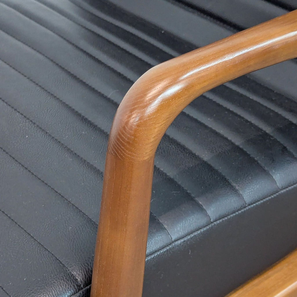 Close-up of Reperch lounge chair's wooden armrest and black leather channel-tufted seat upholstery.