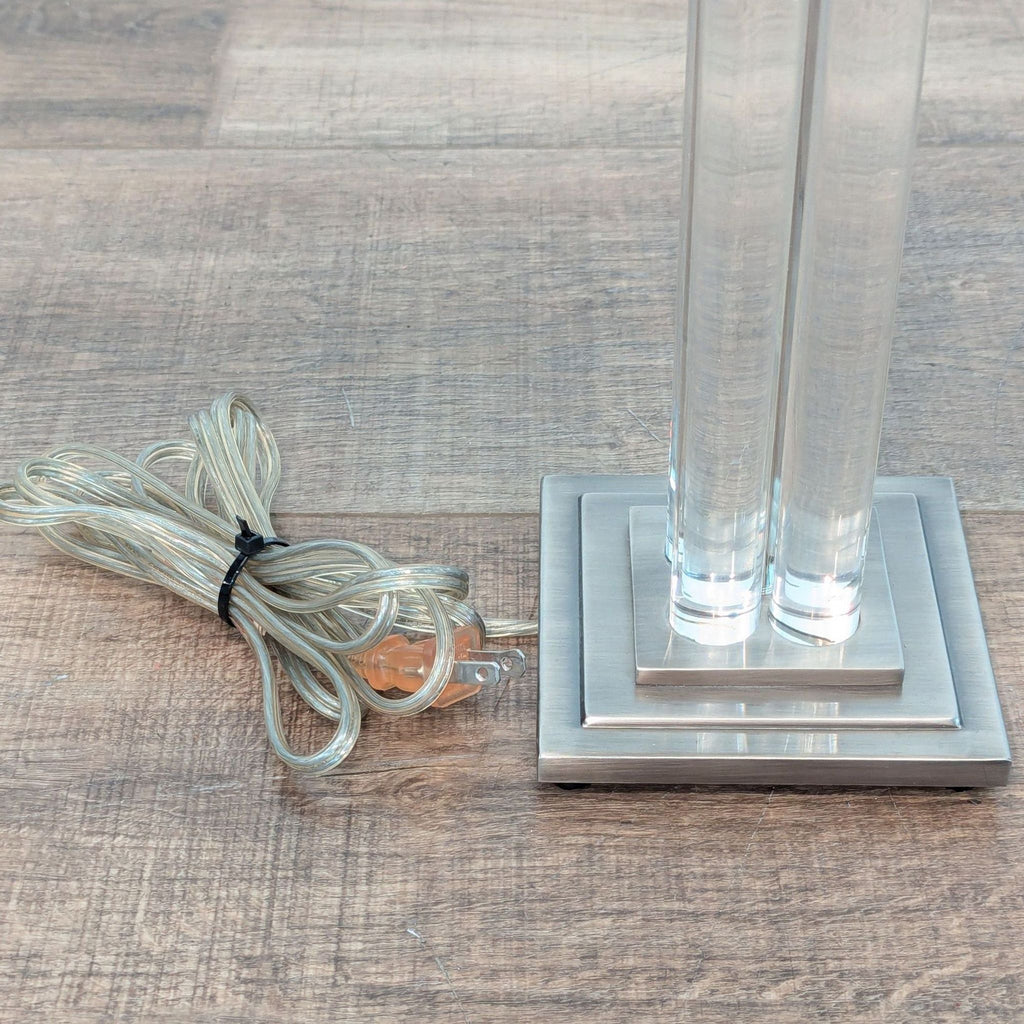 2. Close-up of the lamp's chrome base and clear power cord, showing four acrylic column supports.