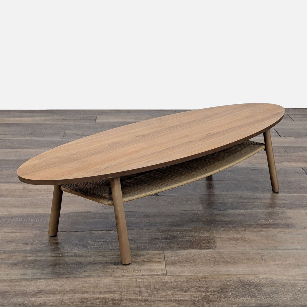 3. Angled view of an oval Reperch coffee table featuring a wood top and a woven raffia lower shelf.