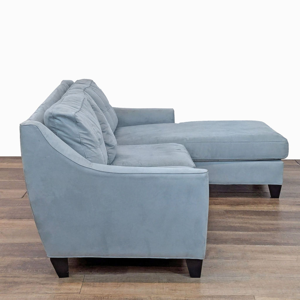 2. Side view of a light blue sectional from Cindy Crawford Home, featuring tufted back, sloped arms, and wood feet.  