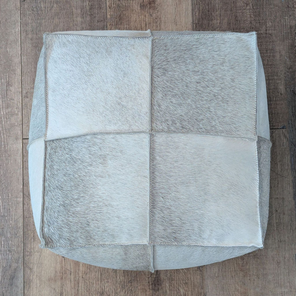 3. Top-down view of a light-colored, patchwork hide CB2 ottoman suitable for use as seating or a footrest.