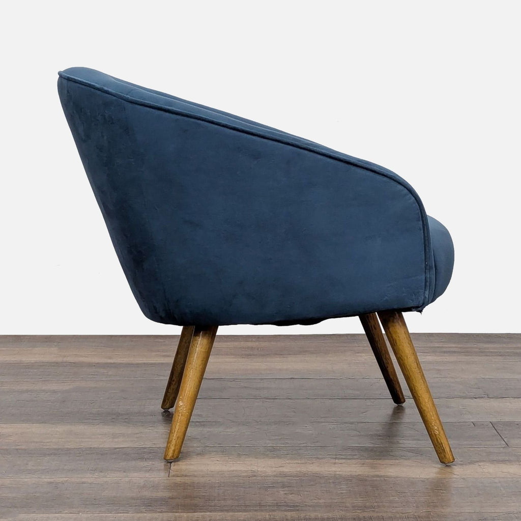 2. Side view of a West Elm lounge chair in blue velvet with slanted wood legs and curved back.