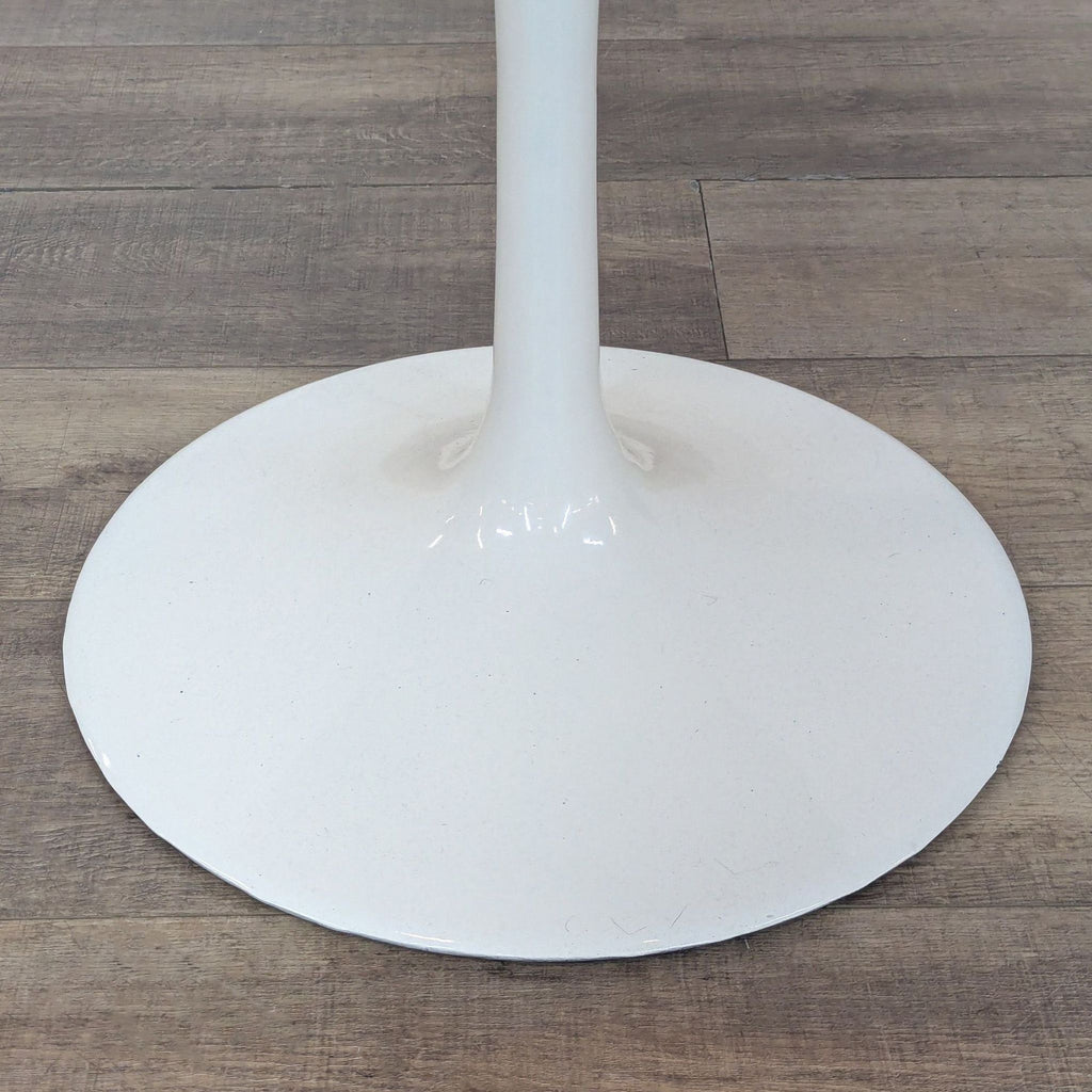 Close-up of the sturdy tulip pedestal base of a white Reperch dining table, placed on wooden flooring.
