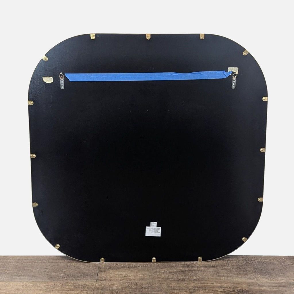 2. Back side of a Crate and Barrel mirror, showing mounting hardware and a sturdy black backing.