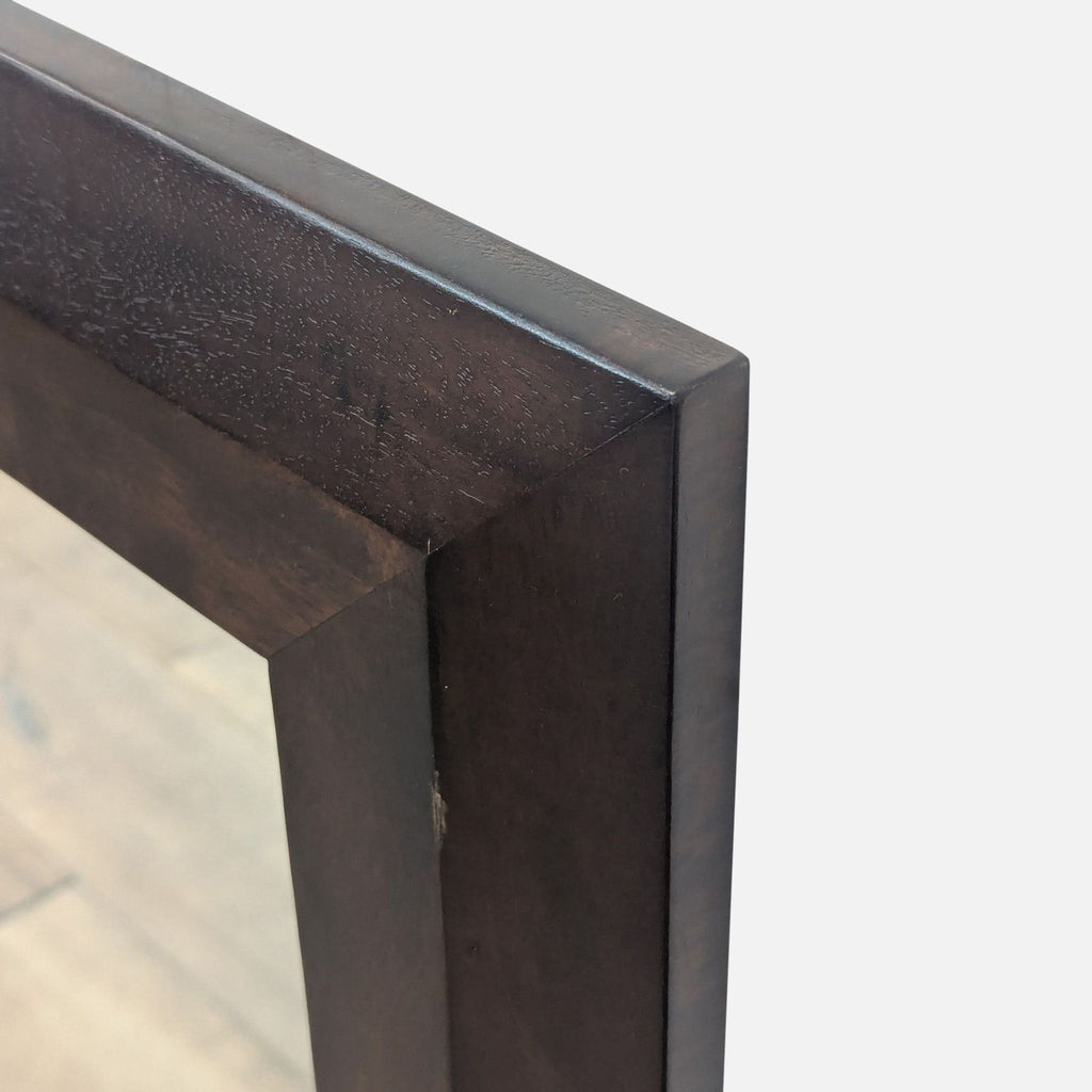 3. Angled detail of the top corner of a Crate and Barrel mirror, highlighting the rich wood frame texture.