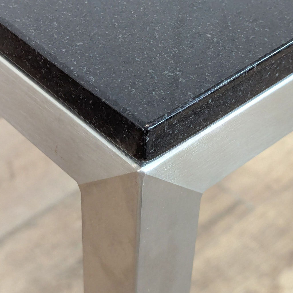 3. Close-up of Room & Board Skinny table corner, showing black top and brushed steel leg detail.