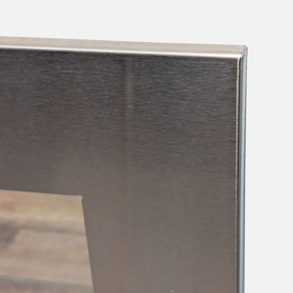 3. Close-up of the brushed metal frame corner of the Room and Board mirror, highlighting its sleek finish.