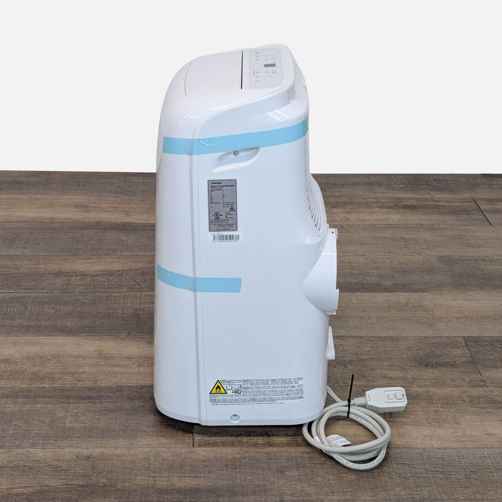 Side view of Toshiba portable air conditioner highlighting controls, vent opening, and coiled power cord on wood floor.