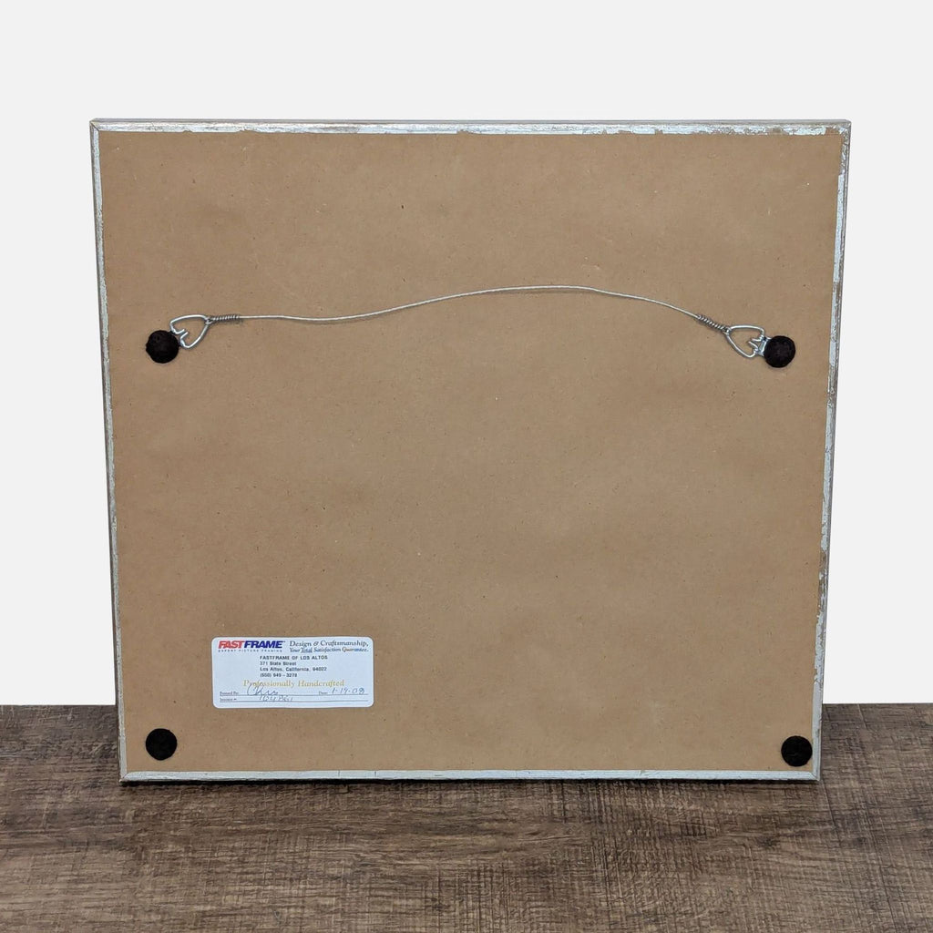 3. Back view of the framed art print showing a hanging wire and label attached to the frame.