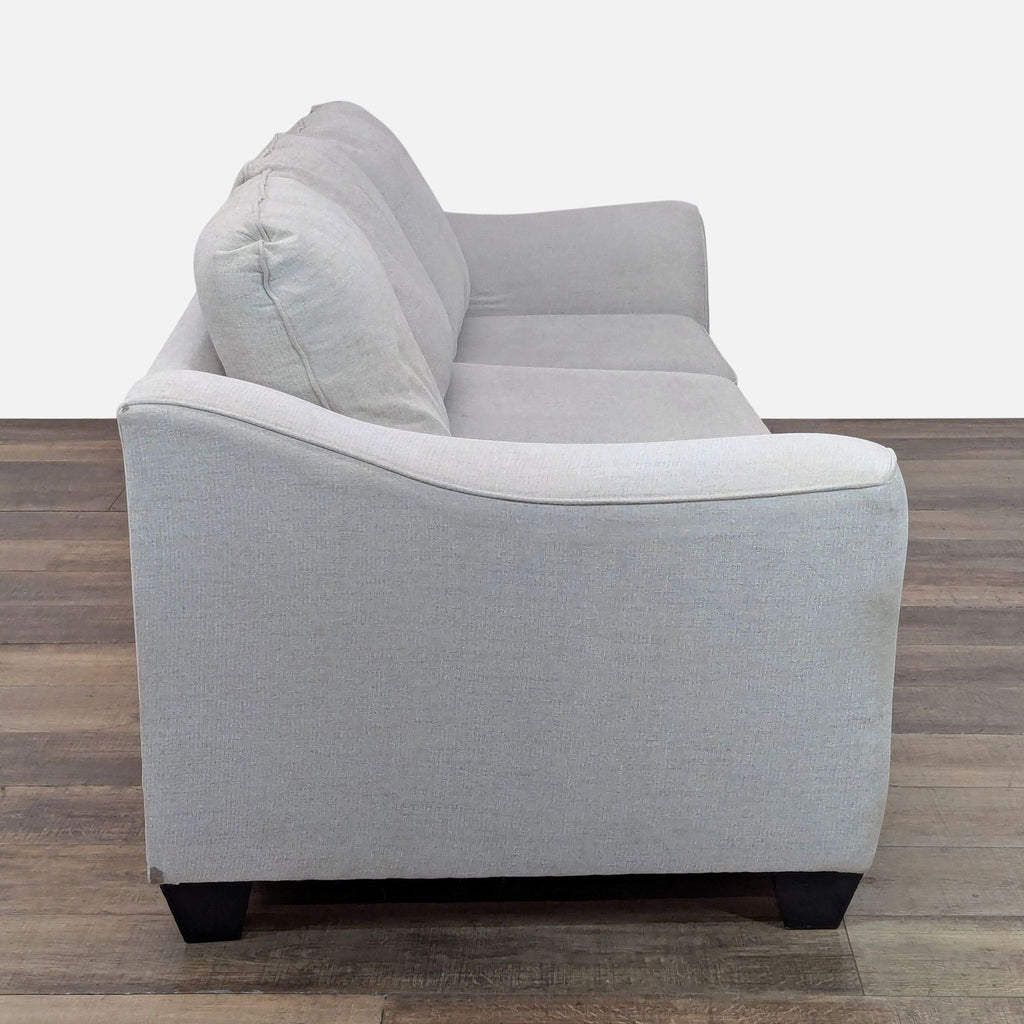 Side view of a modern 3-seat Living Spaces sofa showing curved armrest, three cushions, and wood feet.  