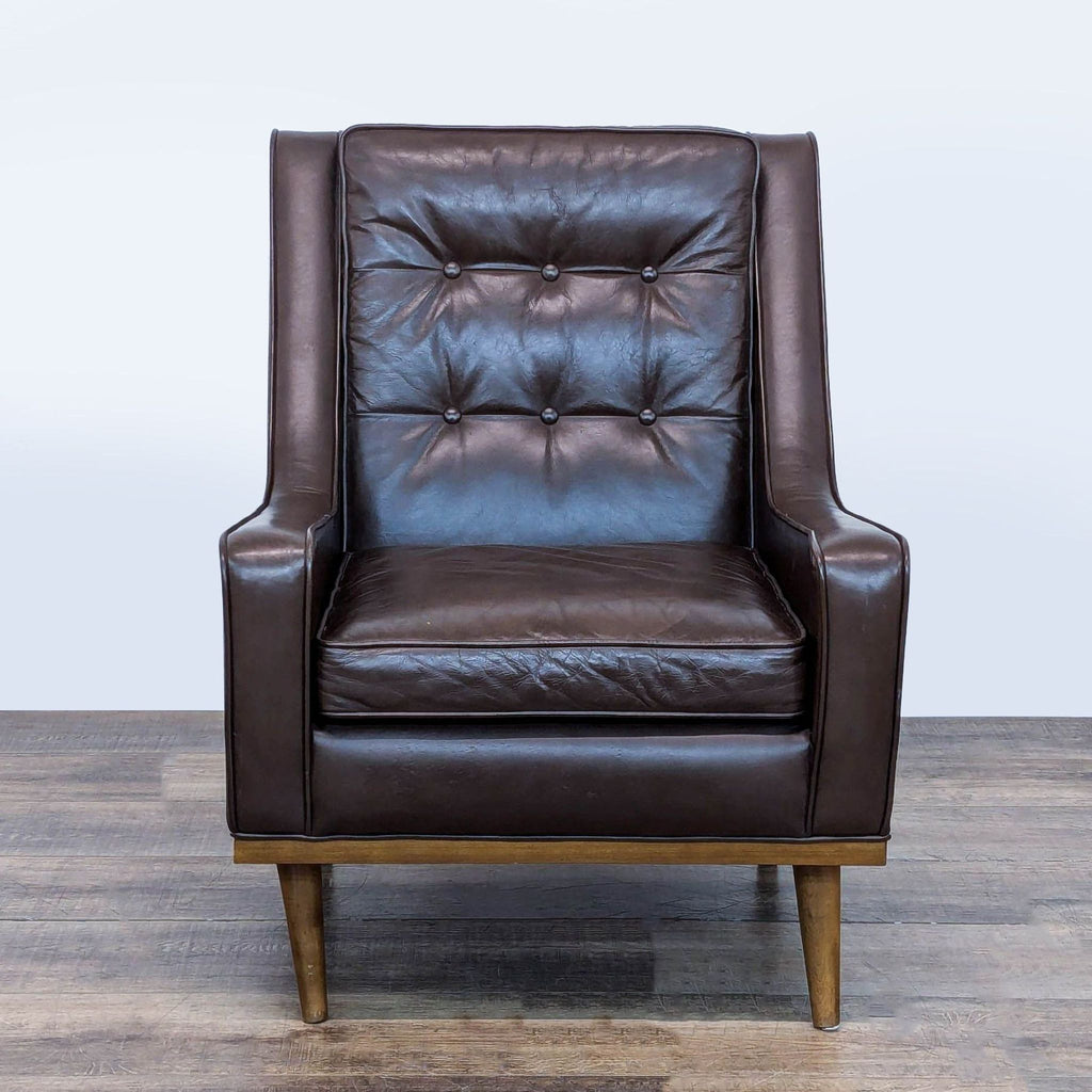 1. Front view of a Reperch lounge chair with brown leather, button tufting, and tapered wood legs.