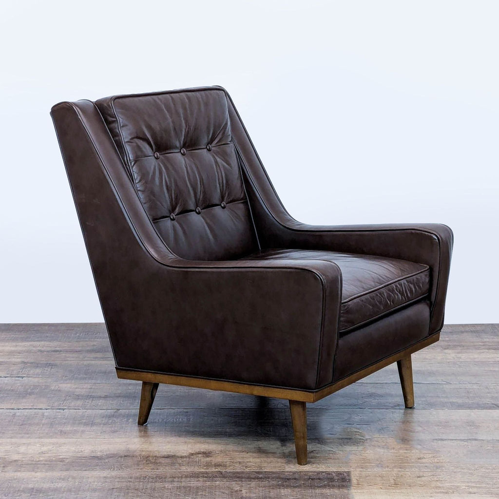 3. Angled view of a brown leather Reperch lounge chair with button tufting and tapered wooden legs.
