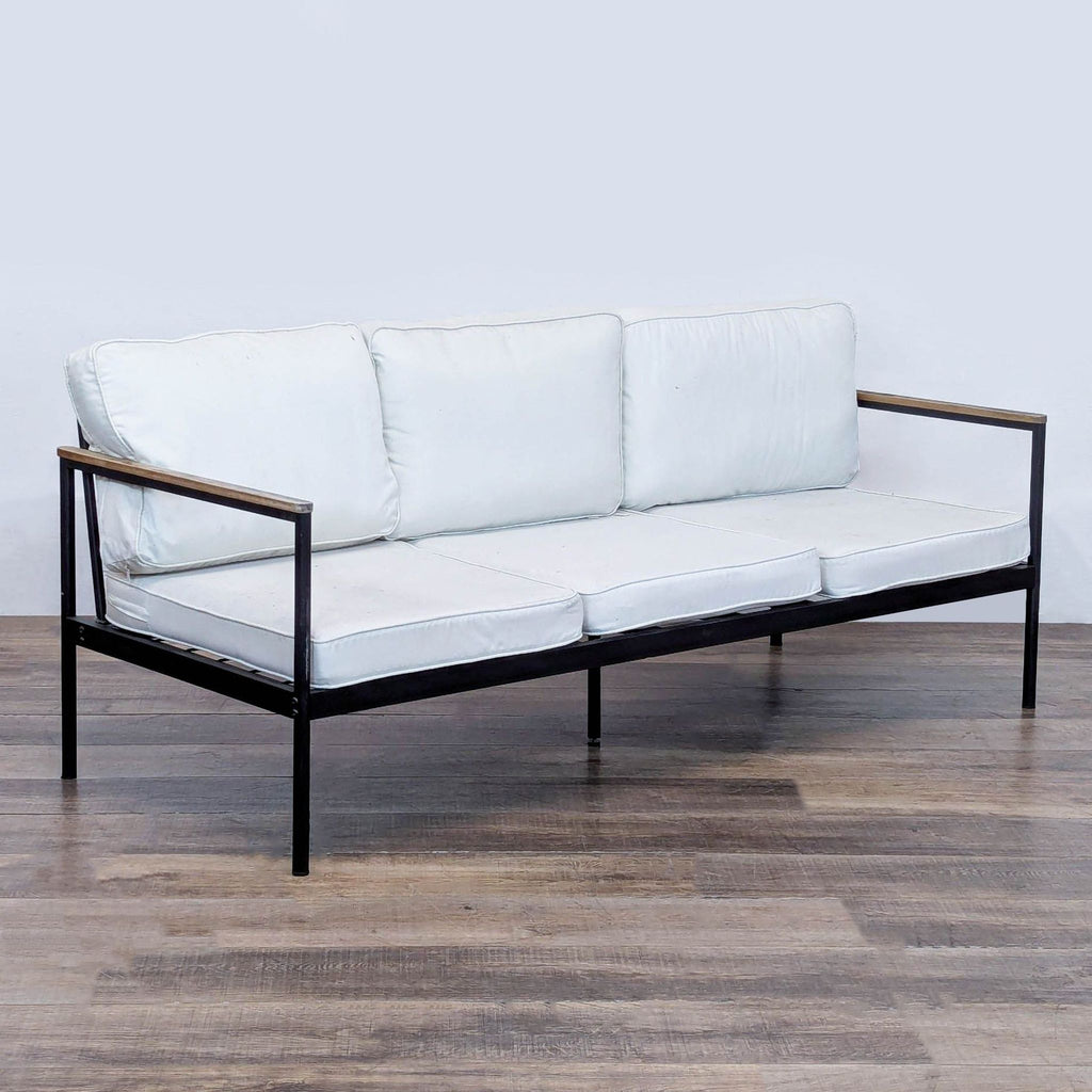 3. Angled view of a Reperch outdoor sofa featuring a black metal frame, wooden armrests, and white removable cushions.