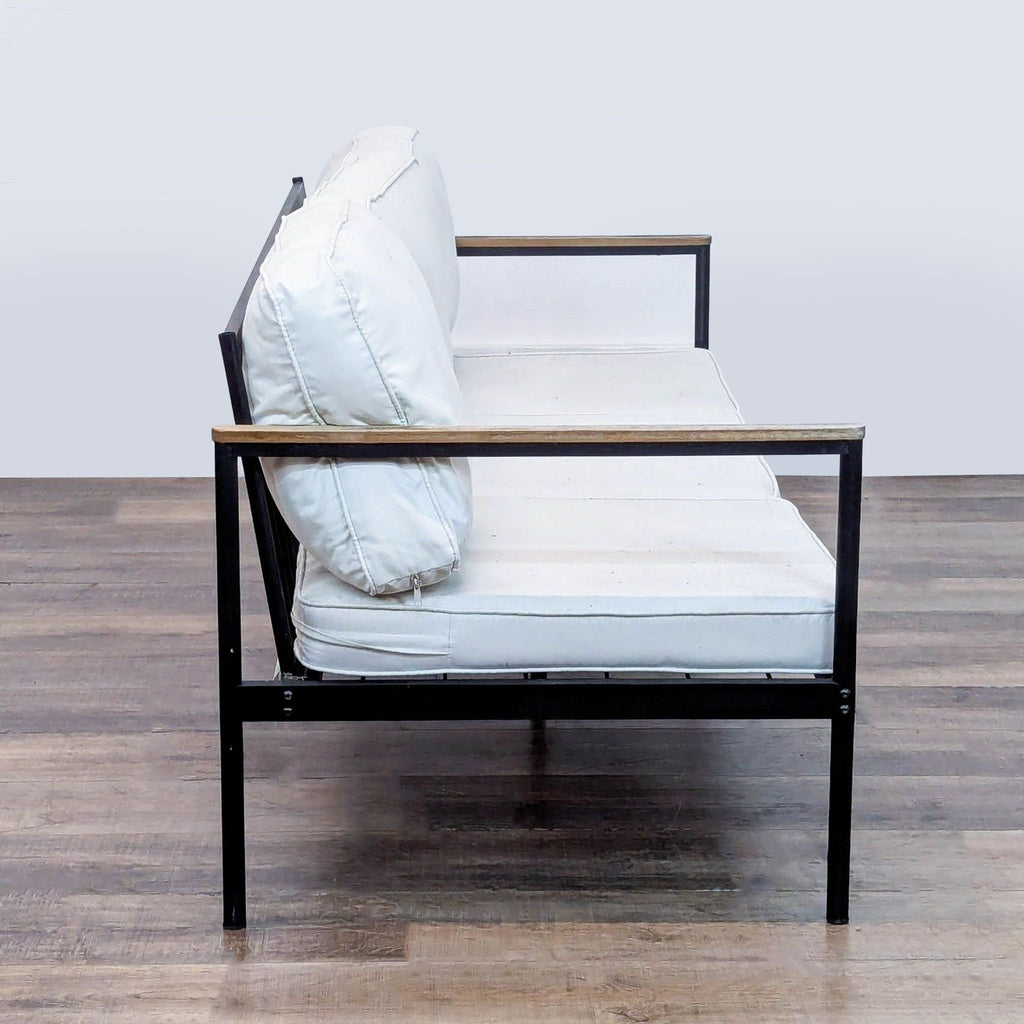 2. Side view of a Reperch outdoor sofa, showing the slim metal frame, wood armrest, and plush removable cushions.