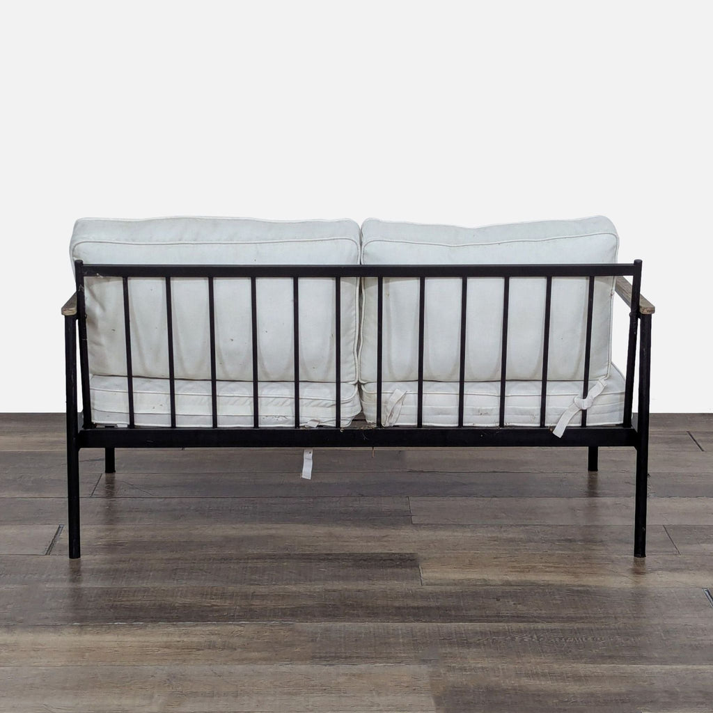 3. Rear view of Reperch chair highlighting slatted metal back, wood armrests, and removable white cushions.