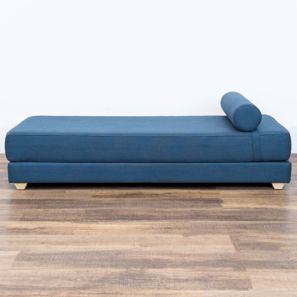 3. Blue CB2 lounge with two mattresses and a cylindrical pillow, shown from the right side, on wooden flooring.