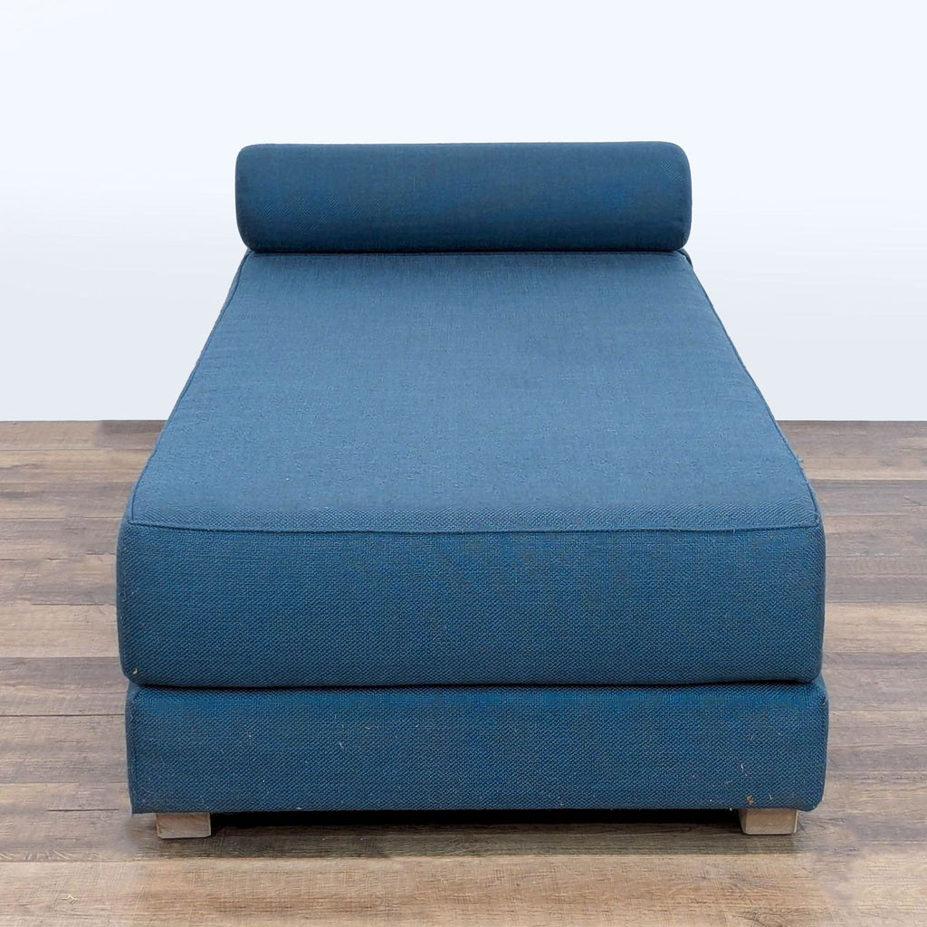 1. Front view of a blue CB2 lounge with a cylindrical headrest and stacked double mattresses on a wood floor.