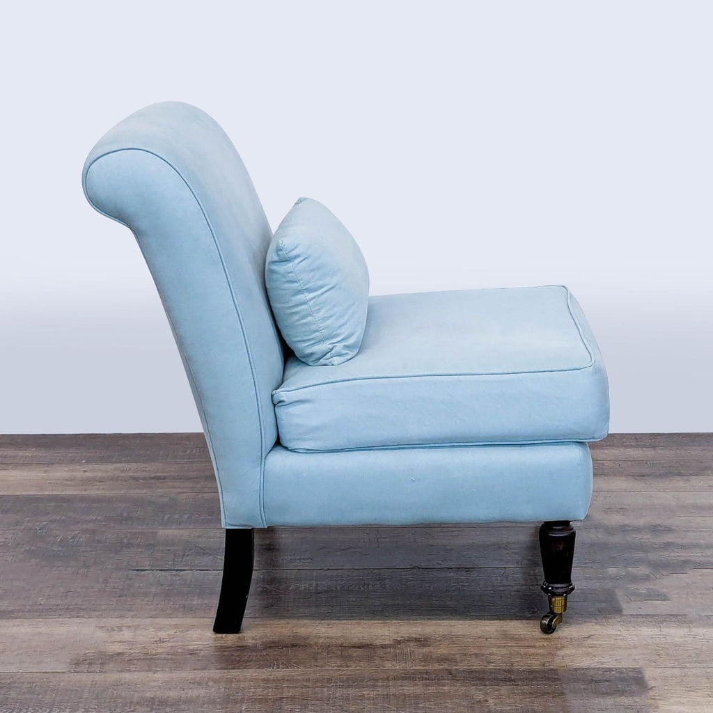 Side profile of Ballenger lounge chair featuring a rolled back, soft fabric upholstery, and wood legs with brass castors.  