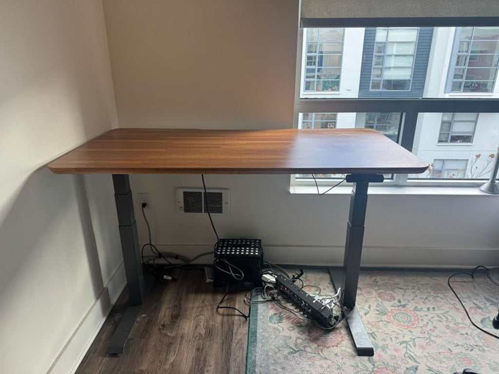 1. Varidesk adjustable standing desk with wood finish top and black metal legs, placed by a window and wall outlet.