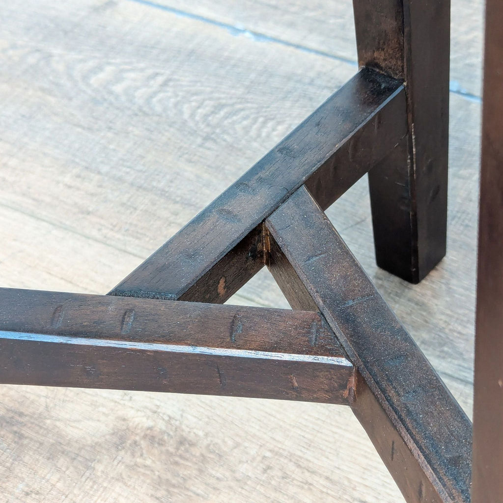 Close-up of Reperch stool’s dark wood triangular leg support, highlighting construction details and finish.