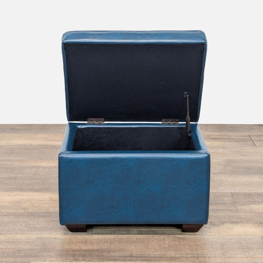 2. Reperch blue ottoman with open hinged lid displaying interior storage compartment on wood floor.