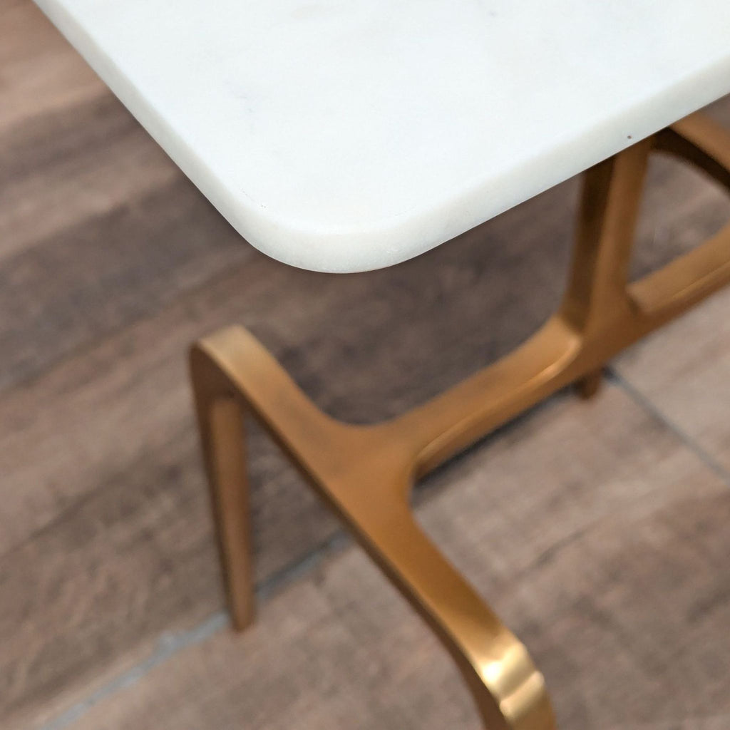 2. Close-up of the CB2 table, showing the smooth white marble top and brass-finished aluminum frame.