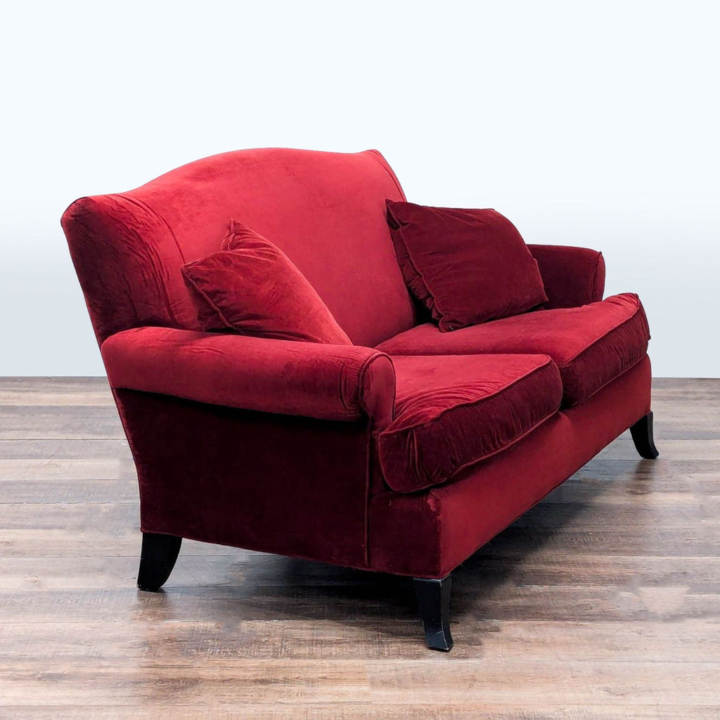 3. Angled view of Crate & Barrel red velvet loveseat featuring rolled arms, wood feet, and cozy transitional design.