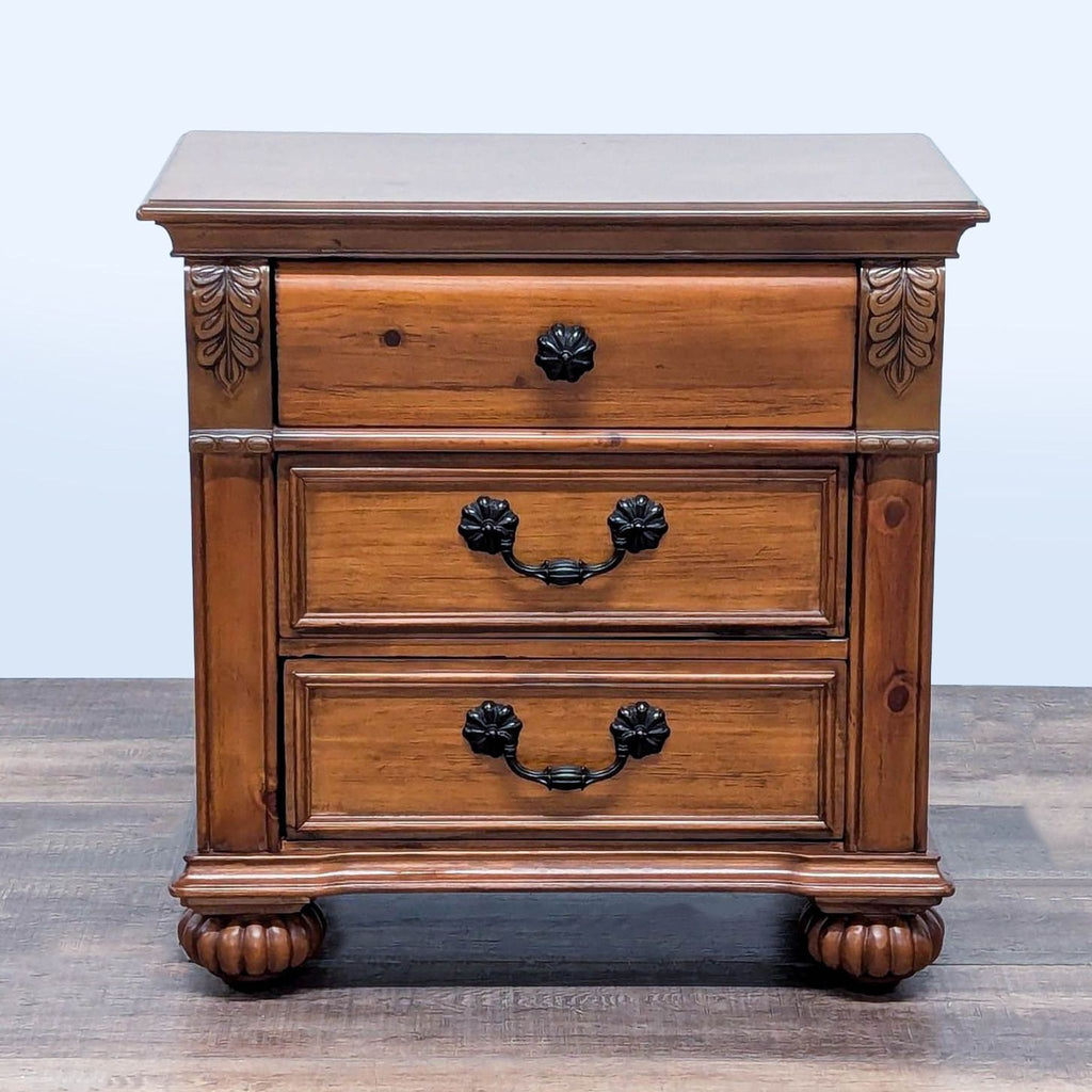 1. Reperch carved end table with three drawers, bun feet, and decorative metal hardware, front view.