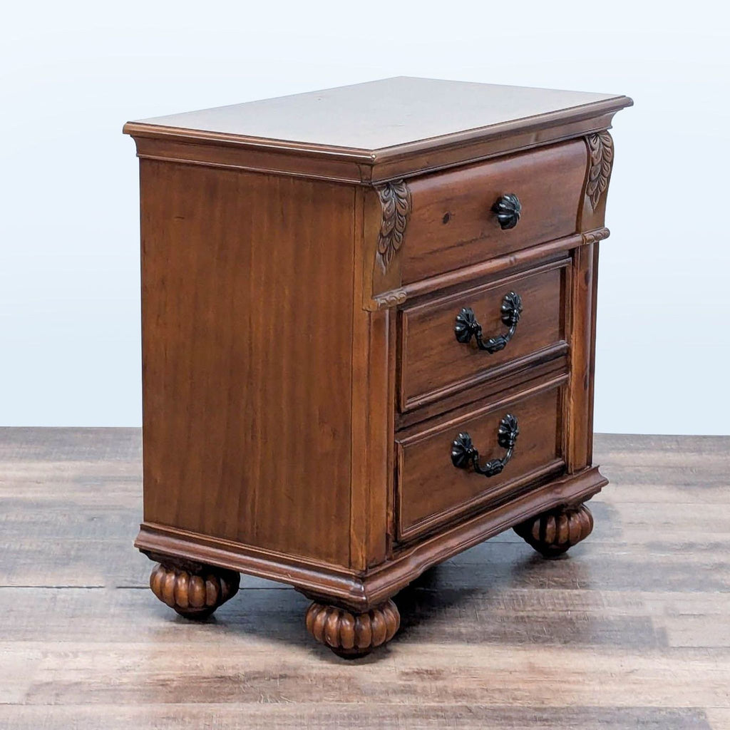 3. Angled view of Reperch nightstand featuring carved accents, bun feet, and black metal handles.
