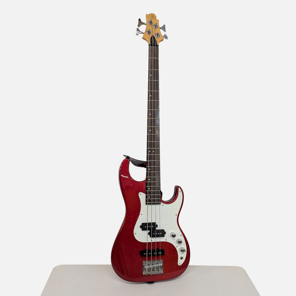 Corsair electric bass guitar with a glossy red finish, four strings, and a white pickguard, standing upright.
