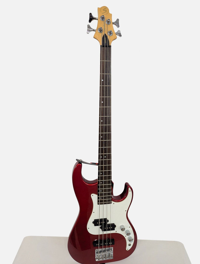 Closeup of a Corsair electric bass guitar’s red body, white pickguard, and control knobs, showcasing build detail.