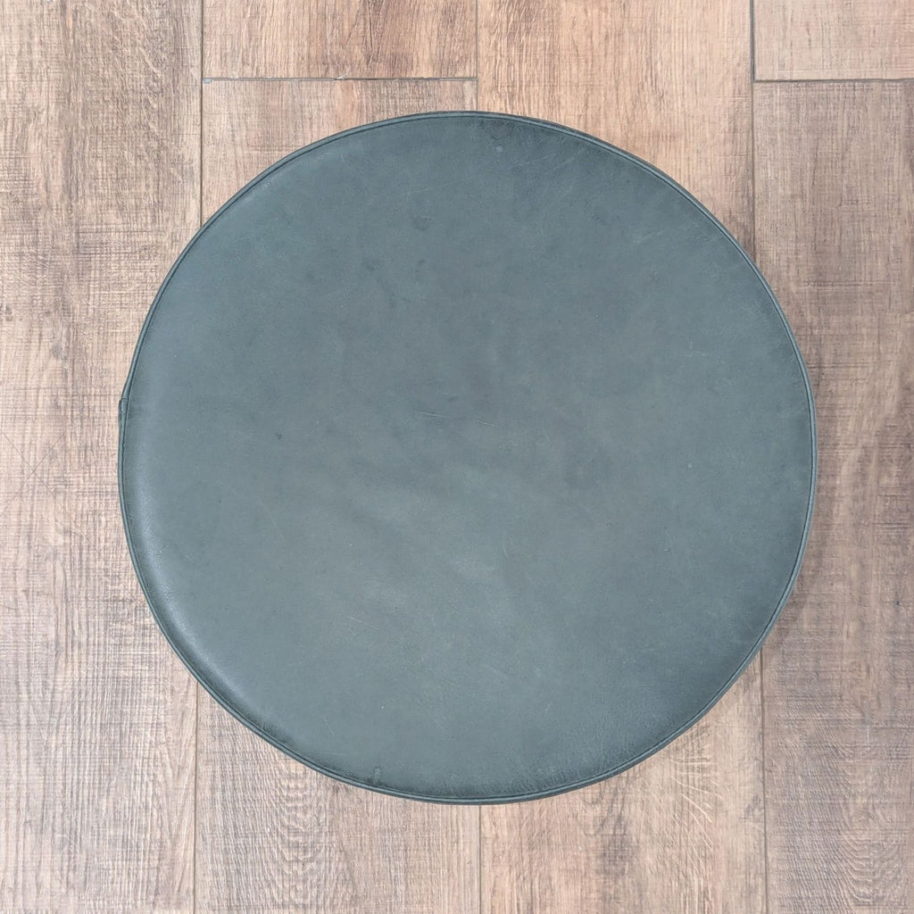 2. Top-down view of a circular Blu Dot ottoman in smooth gray leather, placed on wooden flooring.  