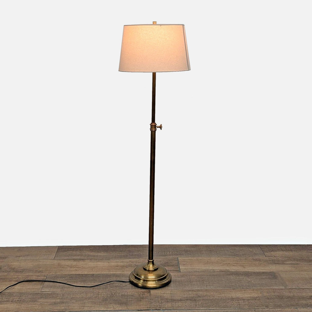 Gold tone adjustable floor lamp with a fabric shade, standing on a wooden floor, Pottery Barn Lighting.