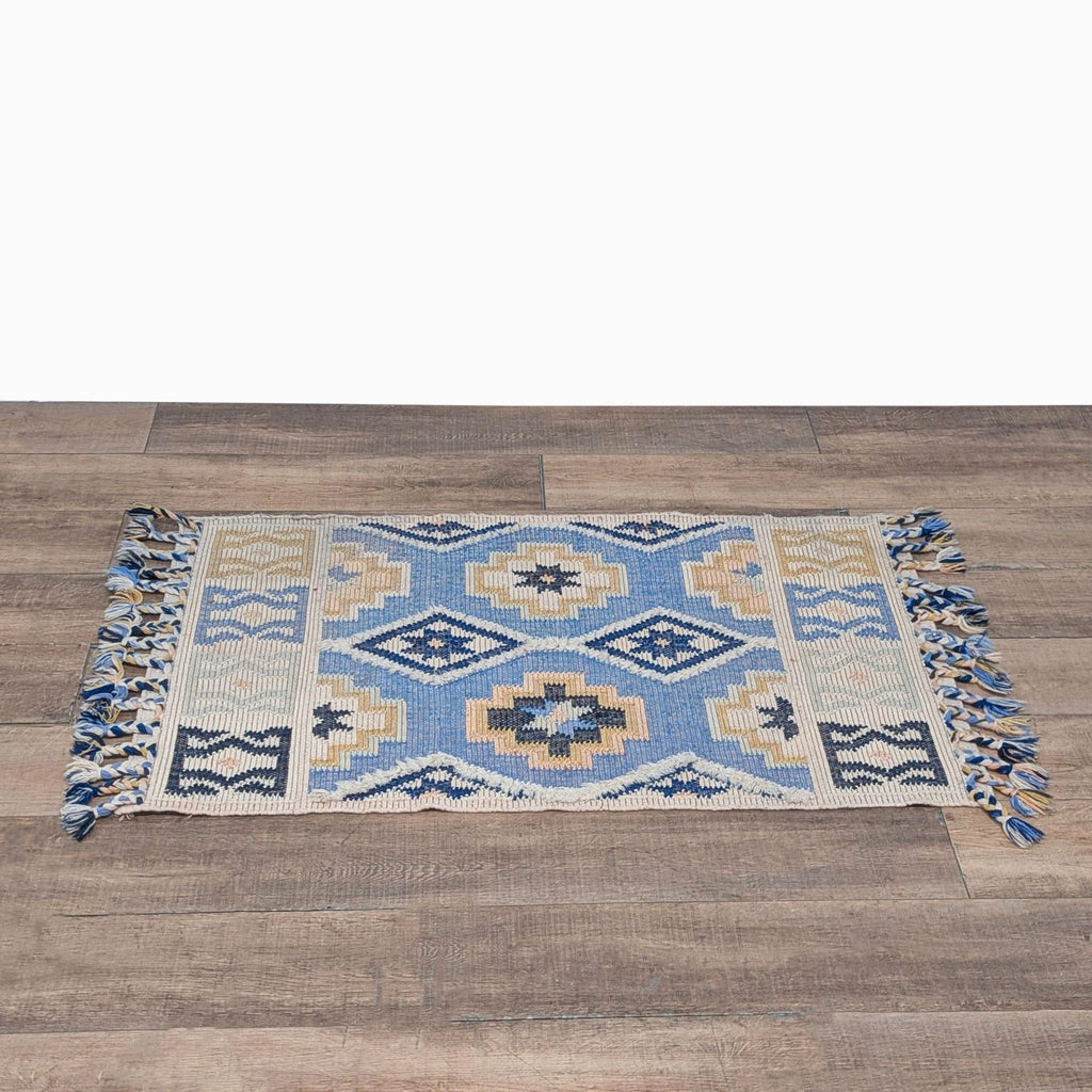 1. Woven Anthropologie rug with geometric blue and tan pattern and braided tassels on each end.