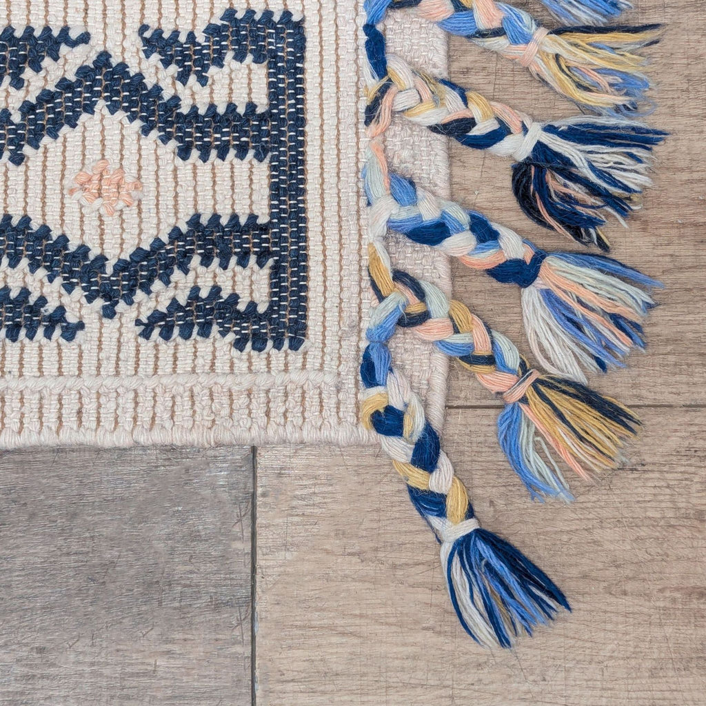 2. Close-up of braided end tassels in blue, yellow, cream, and peach on a woven Anthropologie rug.
