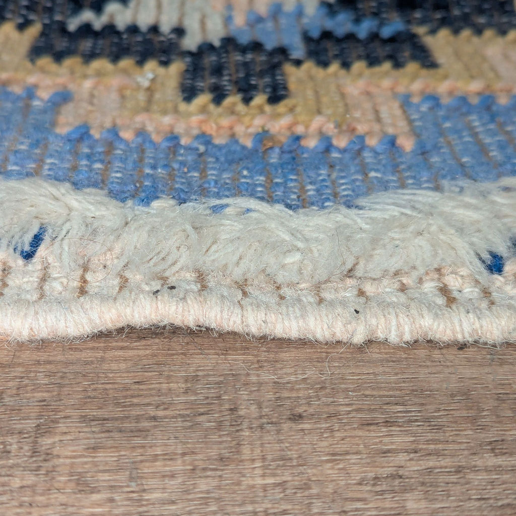 3. Side view of the textured edge and woven fibers of a blue and tan Anthropologie polyester blend rug.