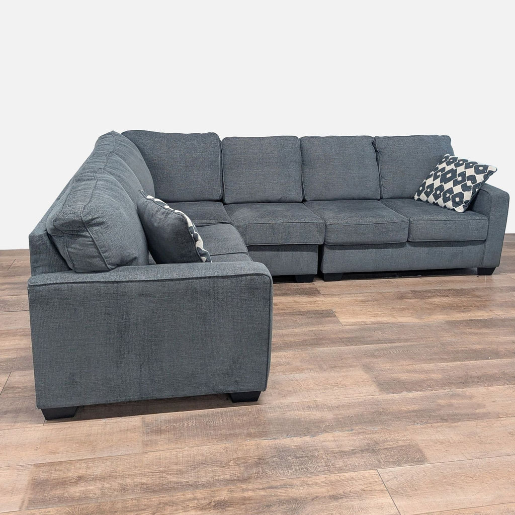 1. Modular dark gray Ashley sectional with plush cushions, wood block feet, and patterned accent pillows.