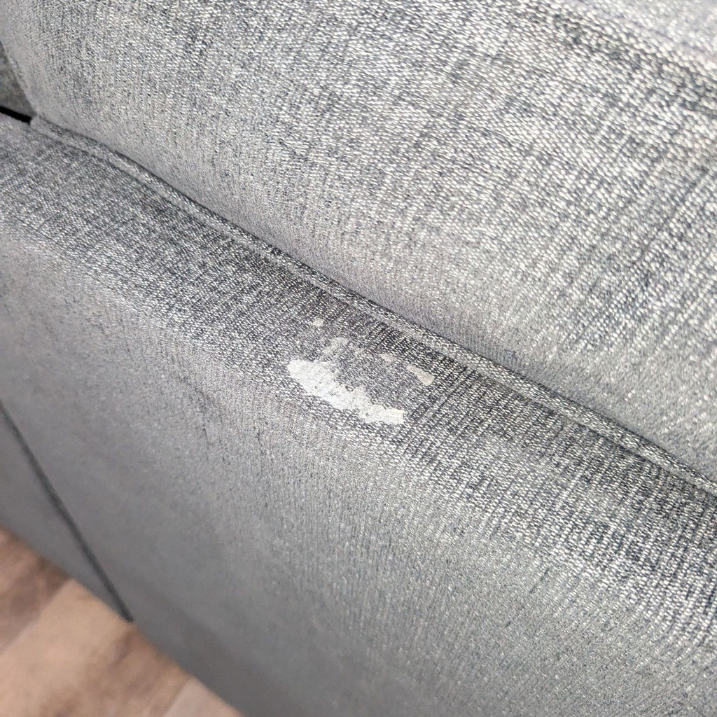 3. Close-up of sectional's dark gray upholstery showing wear with a visible fabric flaw or stain.