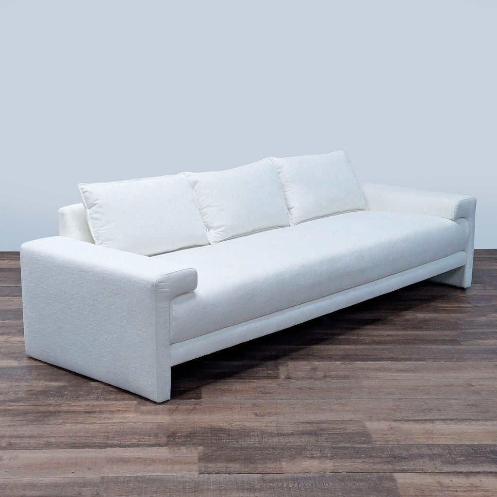 2. Angled view of a white CB2 3-seat sofa with plush cushions and minimalist design on a wood floor.