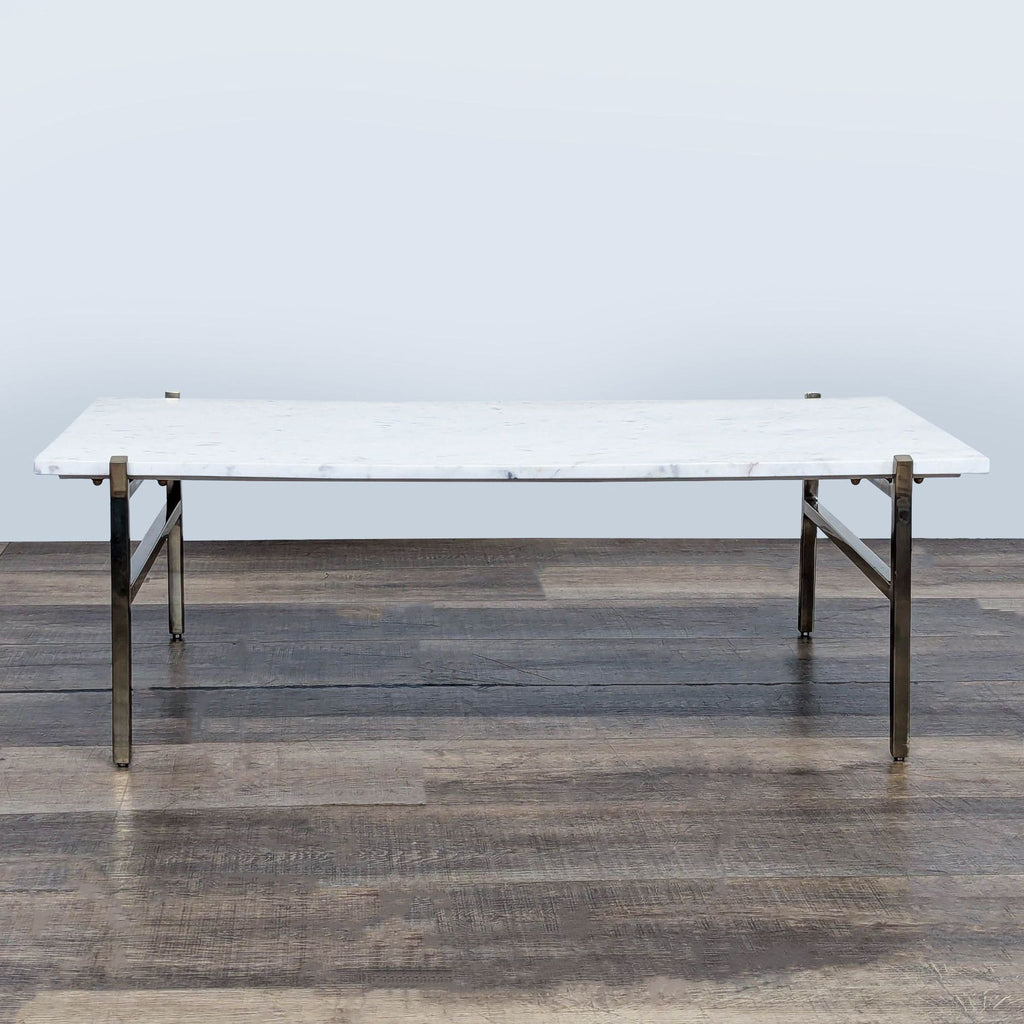 1. CB2 coffee table with a white marble top and metal base, shown on a wooden floor, front view.