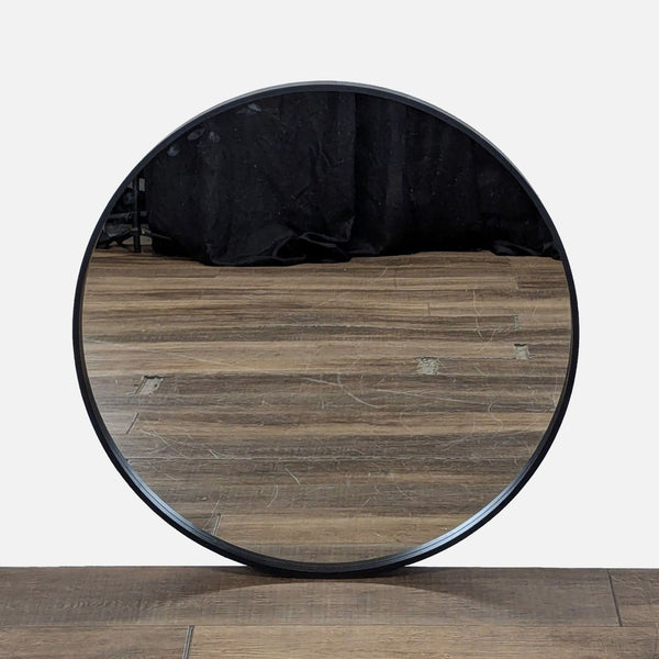 1. EQ3 round mirror with a sleek black frame, reflecting wood floor and dark backdrop, from the Mirror category.