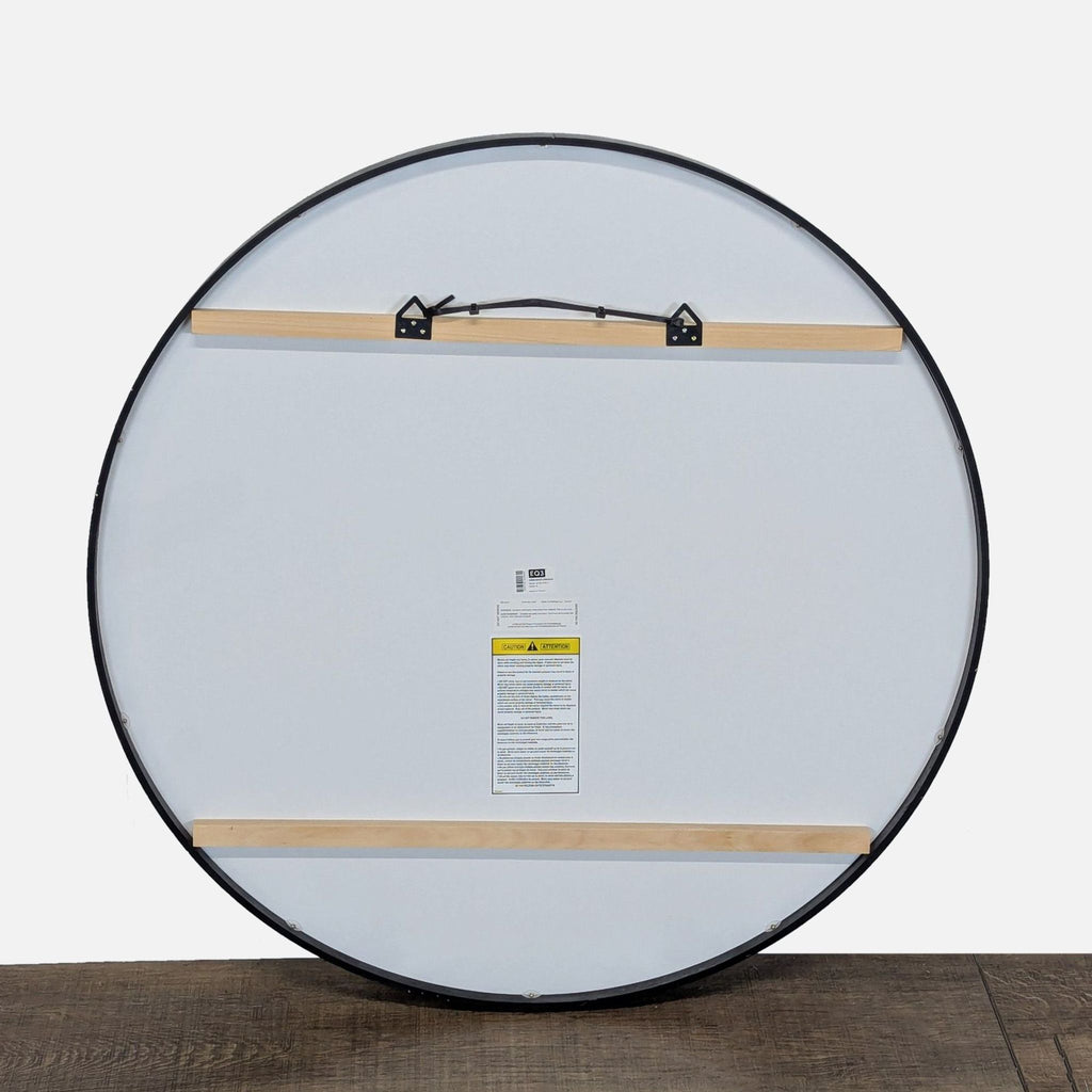 2. Back view of EQ3 black-framed round mirror showing mounting hardware and manufacturer label, Mirror category.