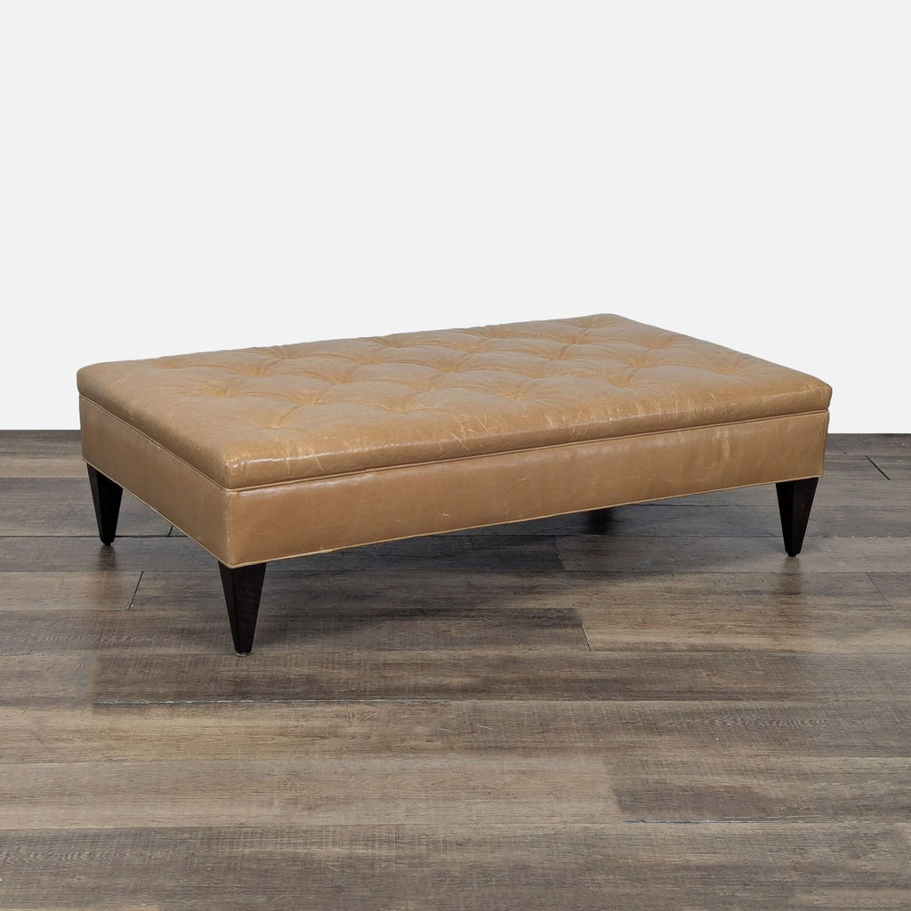 3. Angled view of a tan leather West Elm ottoman with button-tufted seat and dark wooden legs.