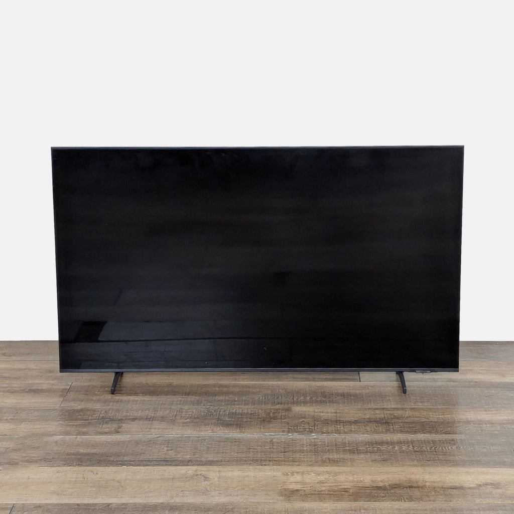 Front view of a Samsung 55-inch QLED 4K Smart TV standing on a wood floor, screen turned off.  