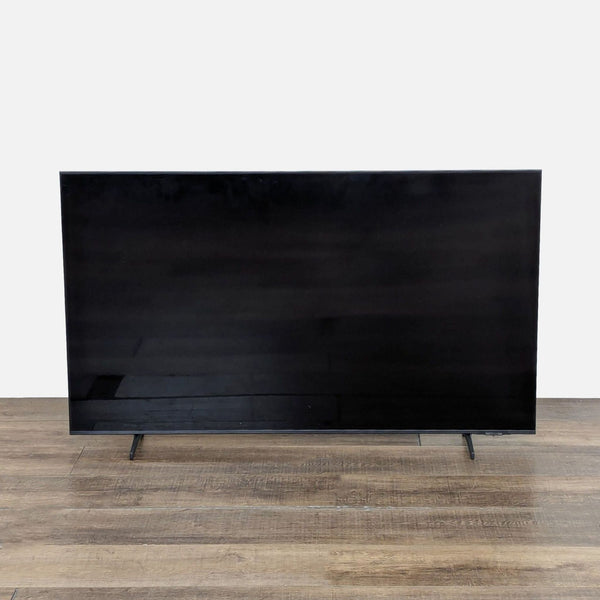 Front view of a Samsung 55-inch QLED 4K Smart TV standing on a wood floor, screen turned off.  