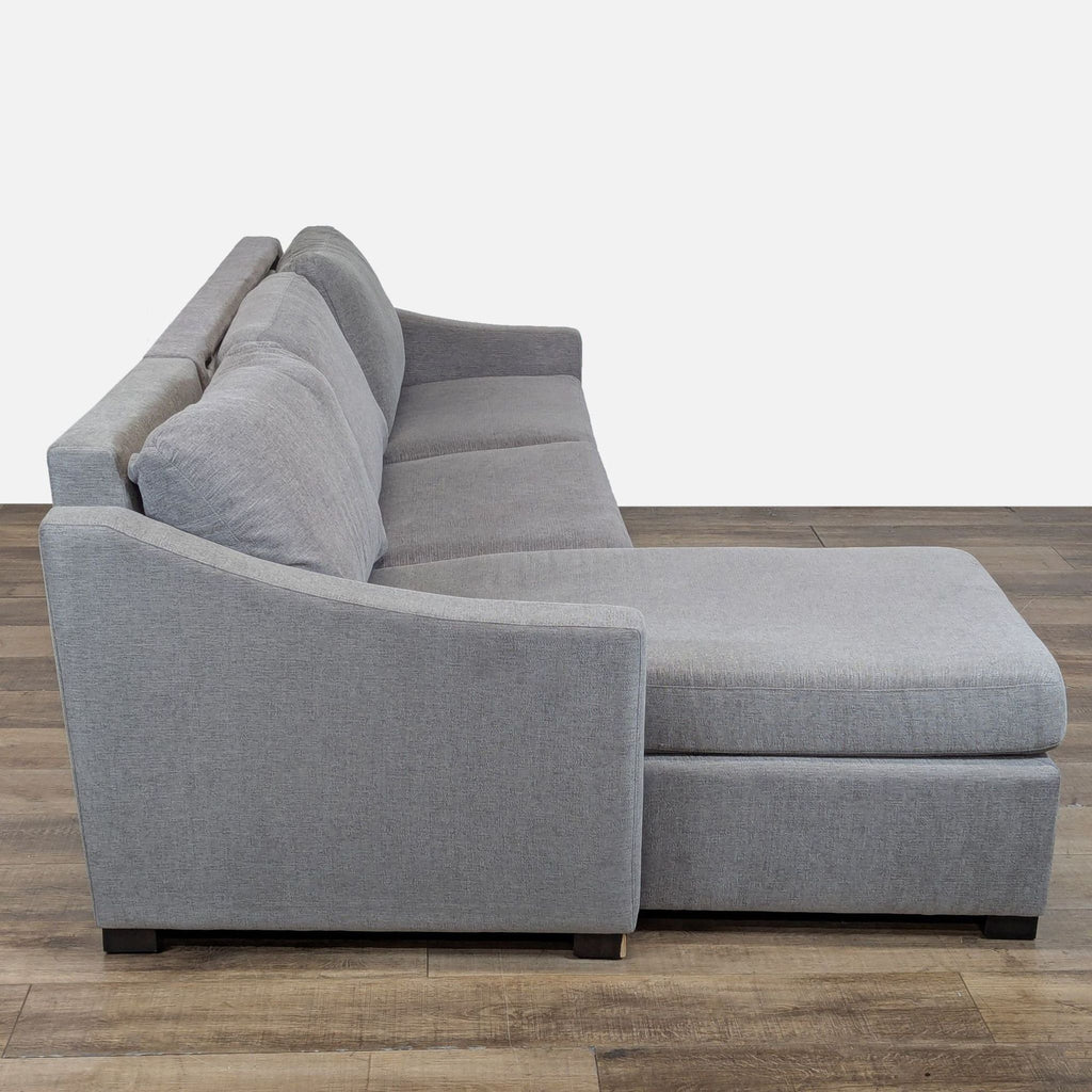 3. Side view of a Crate & Barrel grey sectional sofa with slope arms and plush cushions on wood flooring.