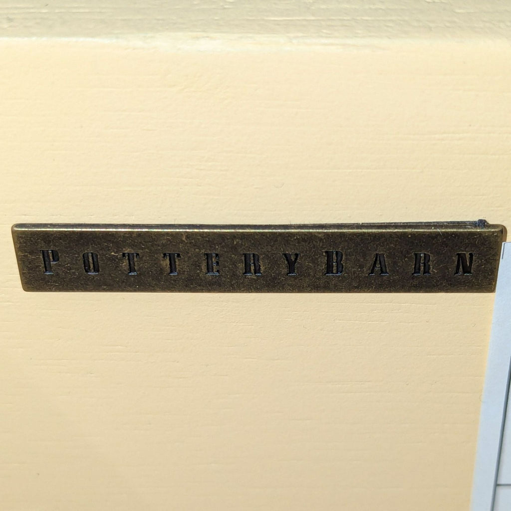 Close-up of a Pottery Barn metal brand label affixed to a cream-colored surface, indicating the dresser's maker.