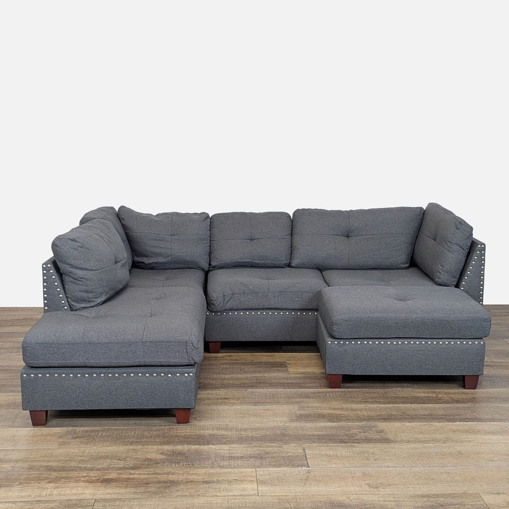 1. Gray upholstered sectional with nailhead trim and a reversible chaise, shown with ottoman on wood floor.