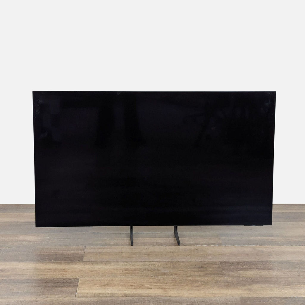 Front view of a 55-inch Samsung OLED 4K Smart TV with slim bezels and a modern stand on wood flooring.  